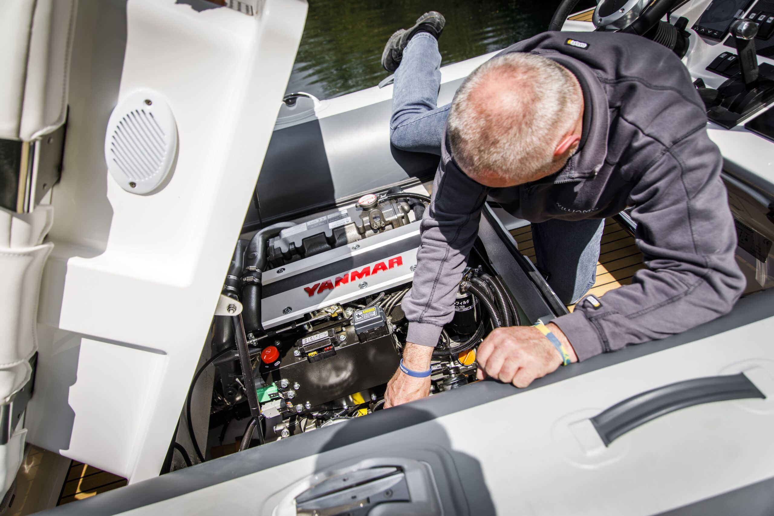 Man leans over boat engine compartment for maintenance.